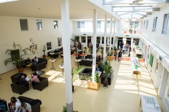 Überblick über den Aufenthaltsraum mit vielen Besuchern, die in Sofas und Sesseln sitzen oder an Stehtischen stehen